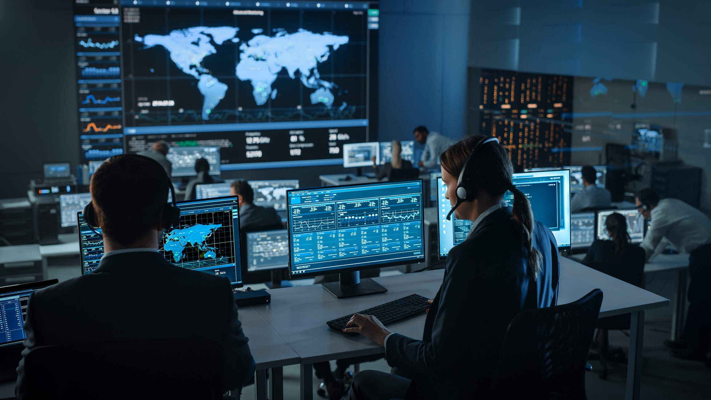 Female Specialist Works on a Computer with Live Ananlysis Feed from a Global Map on a Big Digital Screen. Employees Sit in Front of Displays with Financial Stock Market Trading Info and Big Data.